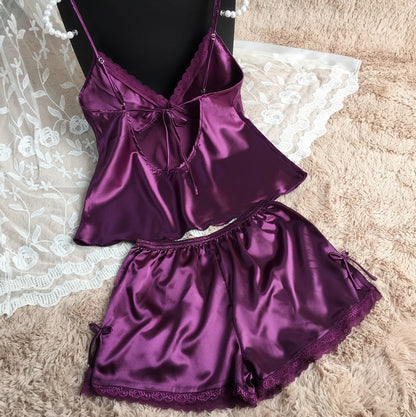 Purple satin camisole and shorts sleepwear set with lace trim on a soft textured background