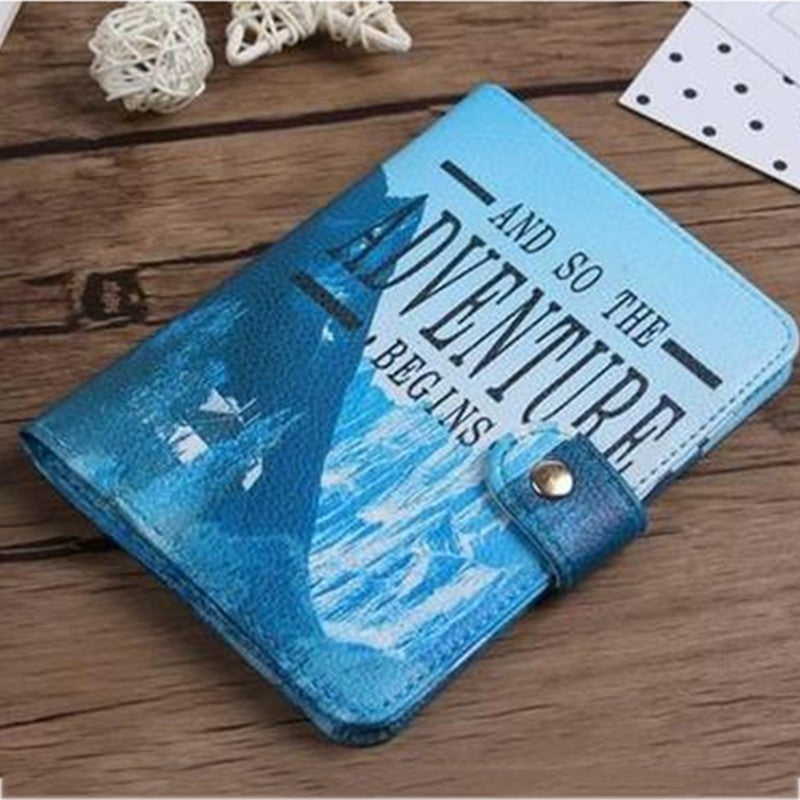 Blue faux leather notebook with 'And So The Adventure Begins' text on wood table, FashionRay