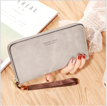 Hand holding a gray zippered wallet with wrist strap on wood table, FashionRay trendy accessory