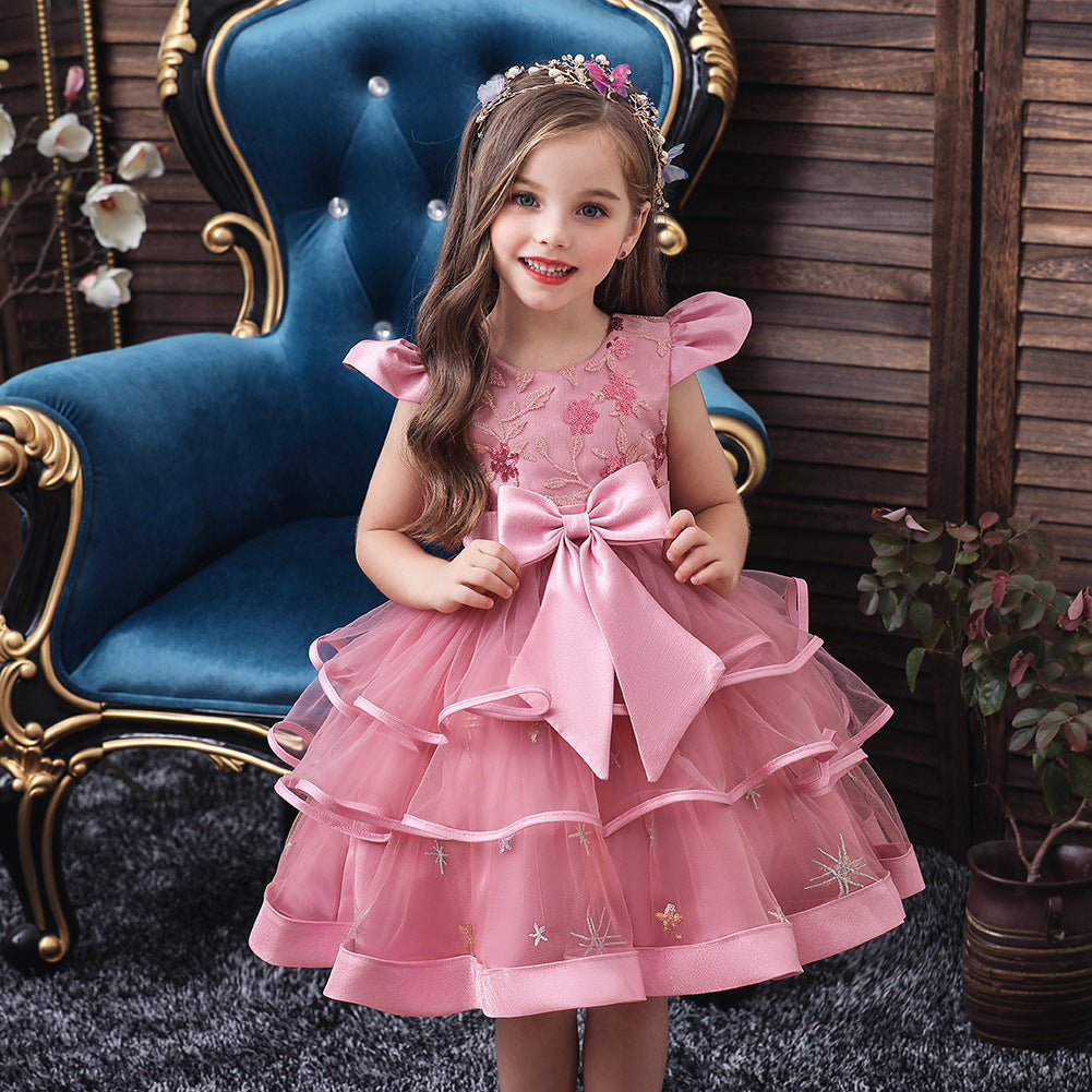 Young girl in pink ruffled dress with large bow poses on blue velvet chair, FashionRay kids formalwear