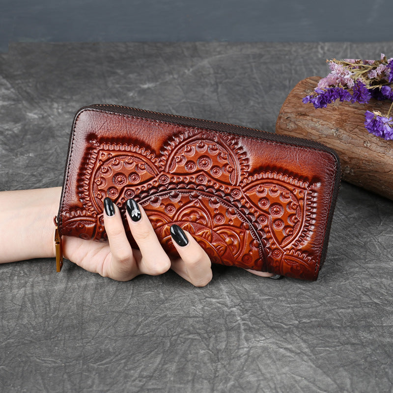 Hand holding embossed brown leather wallet with floral pattern on textured surface, FashionRay
