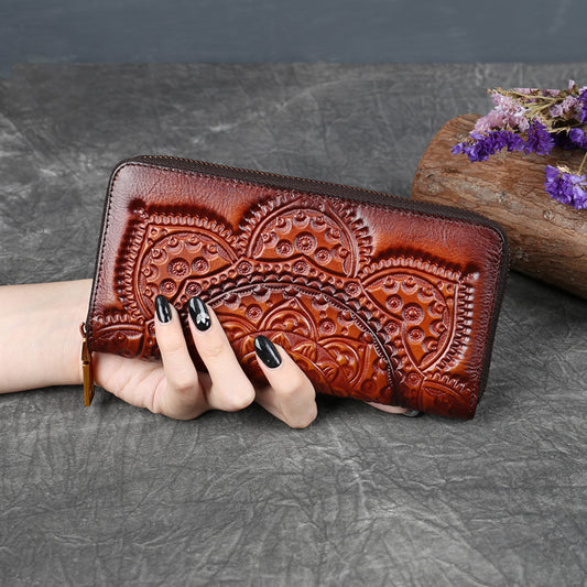 Hand holding embossed brown leather wallet with floral pattern on textured surface, FashionRay