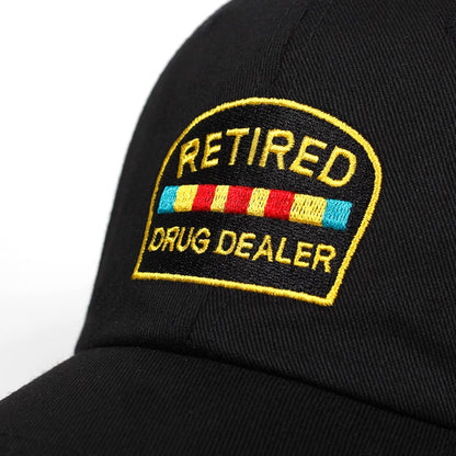 Black cap with yellow embroidered 'Retired Drug Dealer' patch, bold humorous streetwear at FashionRay