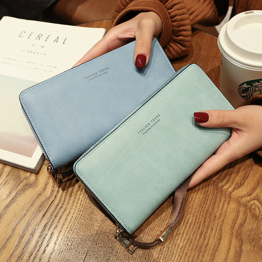 FashionRay pastel blue and mint green zip wallets held on a wooden table with coffee and magazine
