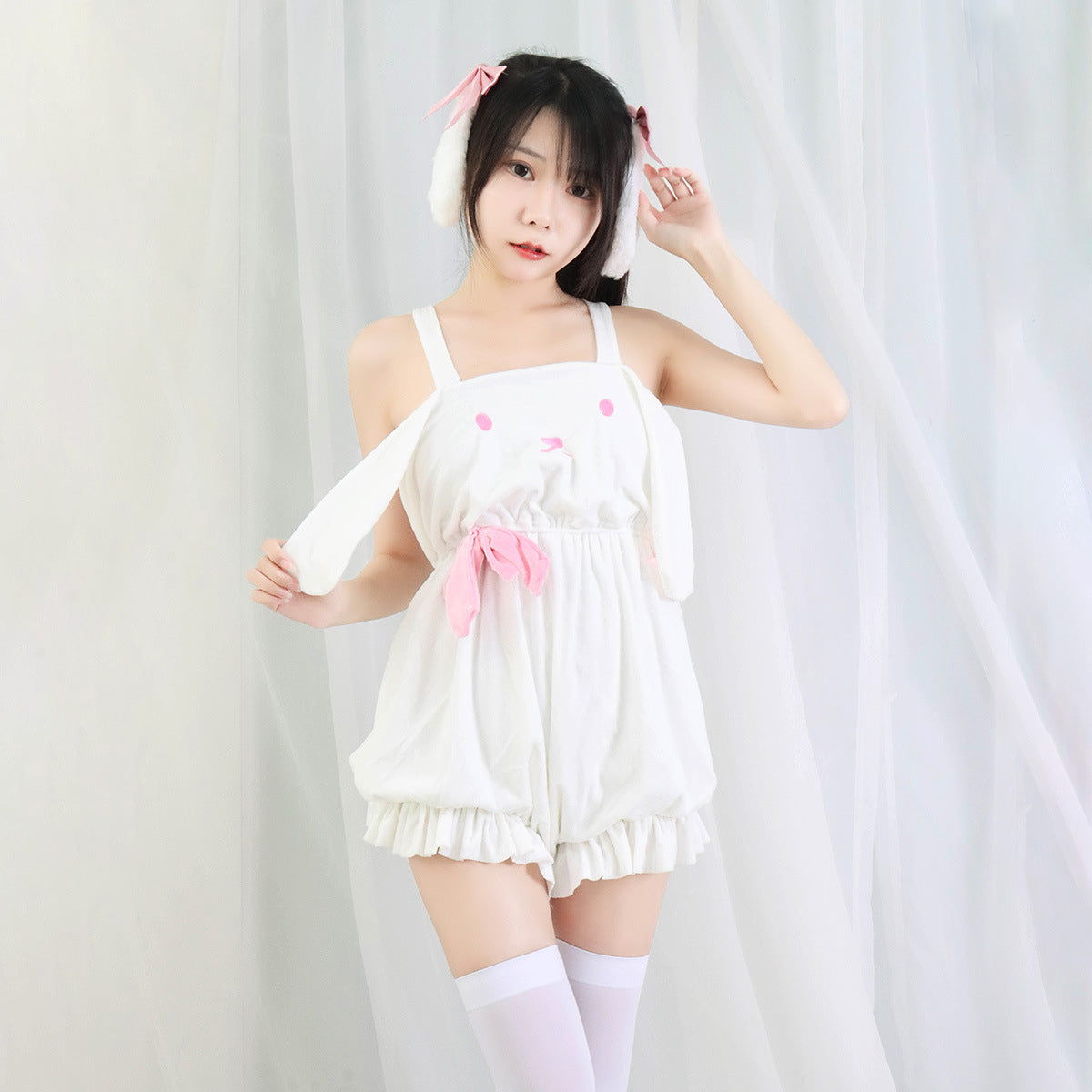 Woman in playful white bunny romper with pink accents and ear headband, soft pastel background