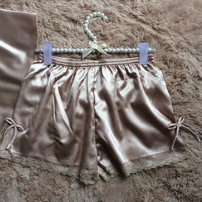 Silky beige satin shorts with lace trim and bow detail, displayed on a plush surface at FashionRay.