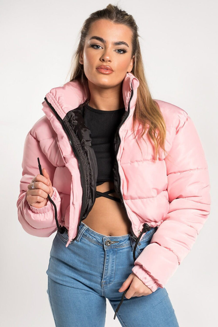 Woman in a pink puffer jacket, black crop top, and blue jeans, FashionRay trendy style