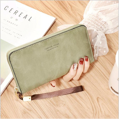 Woman holding green zip wallet with wrist strap on wood table, stylish FashionRay accessory