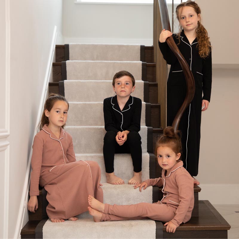 Four children in cozy, stylish pajamas from FashionRay sit and stand on carpeted stairs