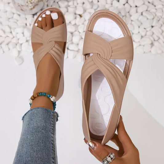 Beige crisscross slip-on sandals on a woman's foot, styled with jeans and beaded anklet, FashionRay