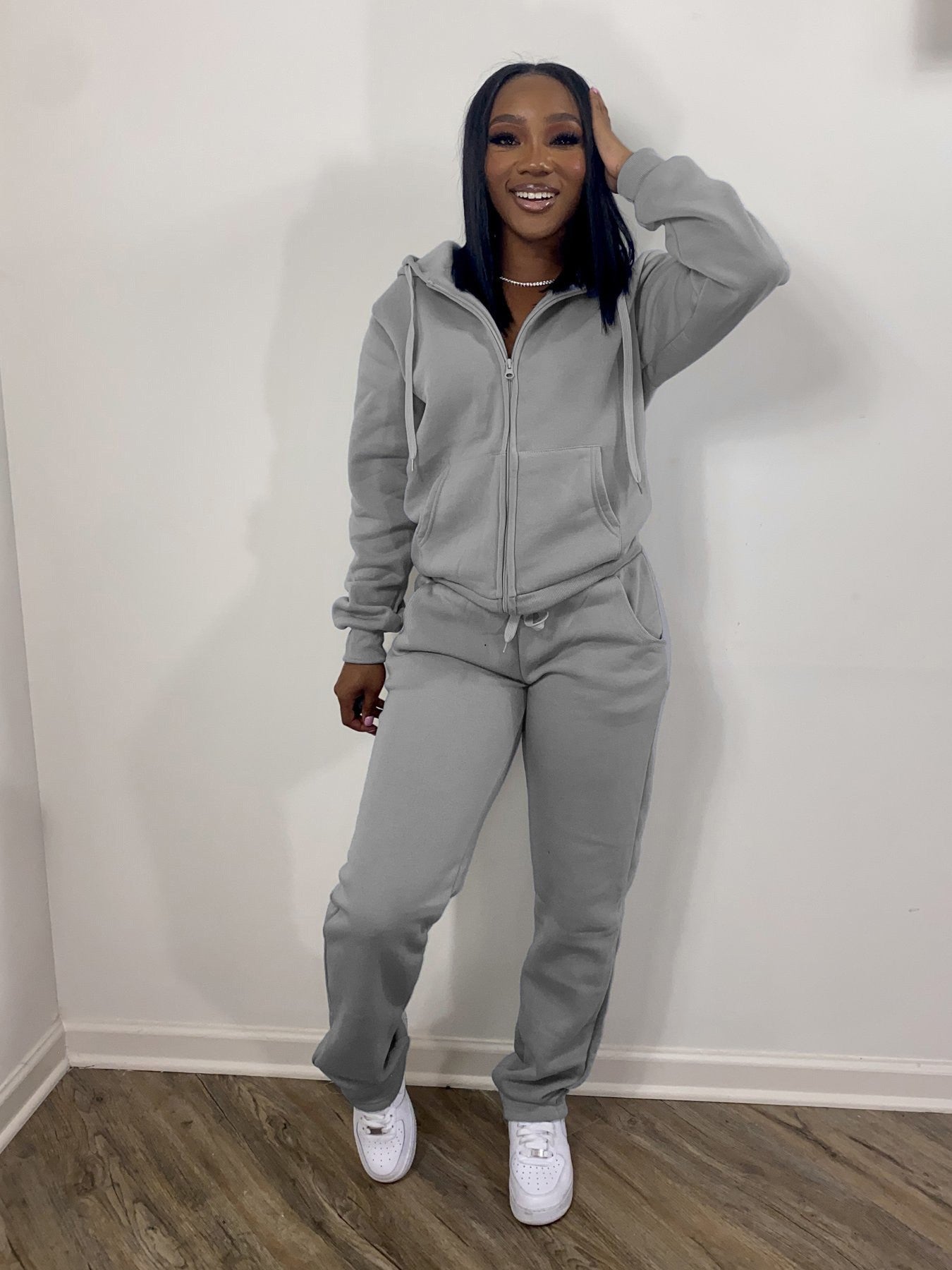 Woman in light gray zip-up hoodie and sweatpants, white sneakers, smiling, FashionRay style