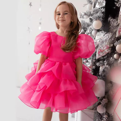 Smiling girl in bright pink ruffle dress by silver Christmas tree, FashionRay style