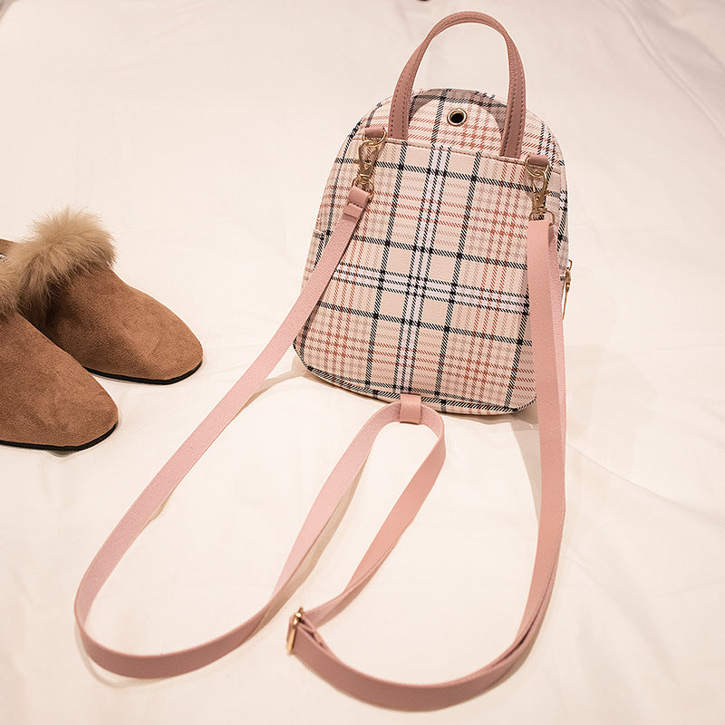 Trendy plaid pink mini backpack with gold hardware on bed next to brown fur-lined slippers