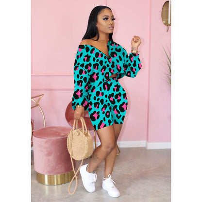 Woman in teal leopard print dress and white sneakers, holding straw bag, in stylish pink room