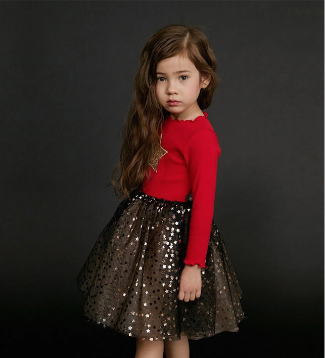 Young girl in a red top and black star-patterned skirt on dark background, FashionRay kidswear