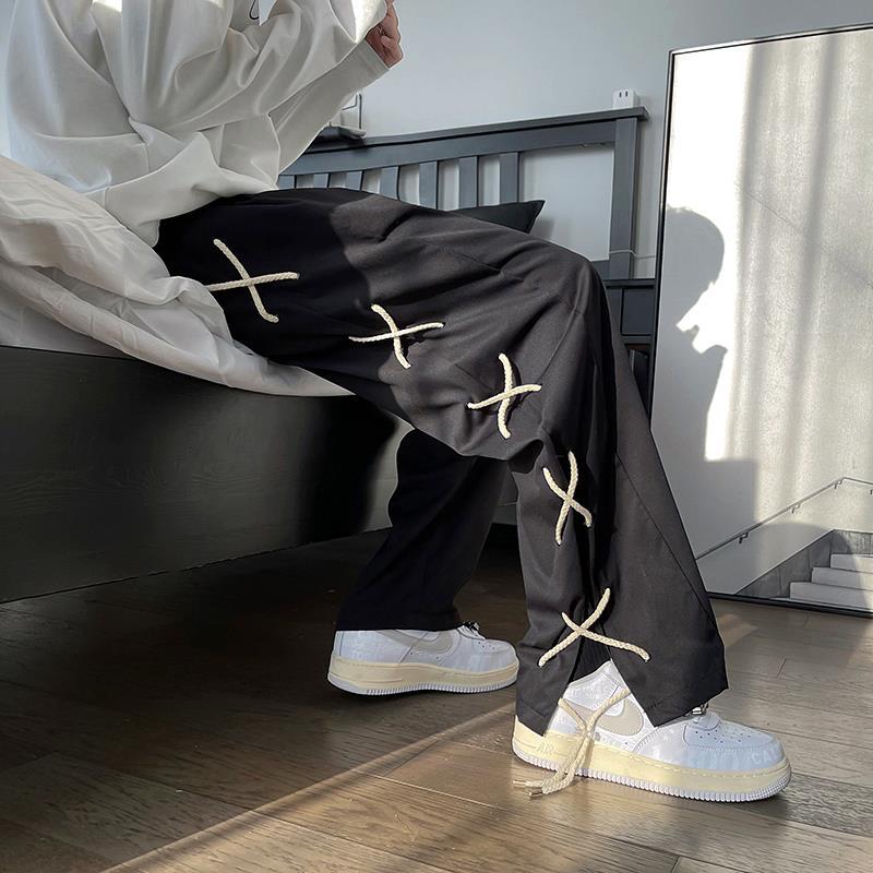 Trendy black pants with rope accents, oversized white shirt, and white sneakers in modern bedroom