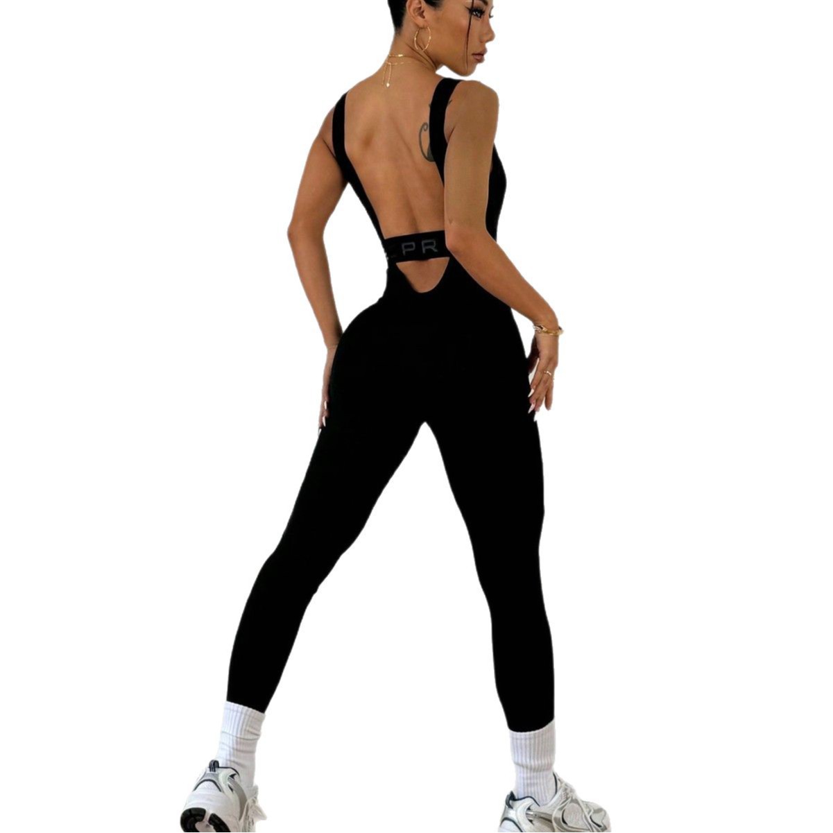 Woman modeling FashionRay black open-back jumpsuit with white sneakers on white background
