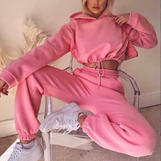 Woman in pink hoodie and joggers set posing on clear chair, trendy loungewear fashion