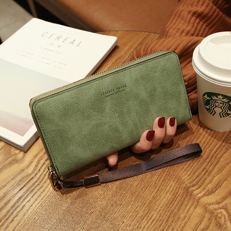 Green faux leather wallet with wrist strap on wood table, near magazine and Starbucks cup, FashionRay