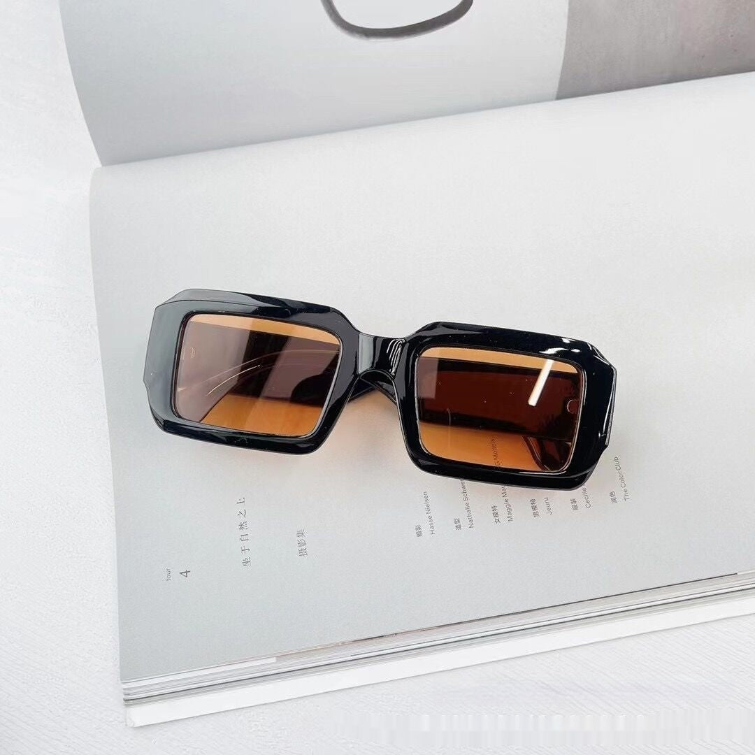 Trendy black square sunglasses with brown lenses on open magazine, FashionRay style accessory