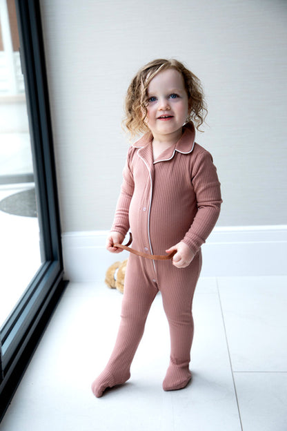 Smiling toddler in a pink ribbed jumpsuit by window, showcasing FashionRay comfort fashion