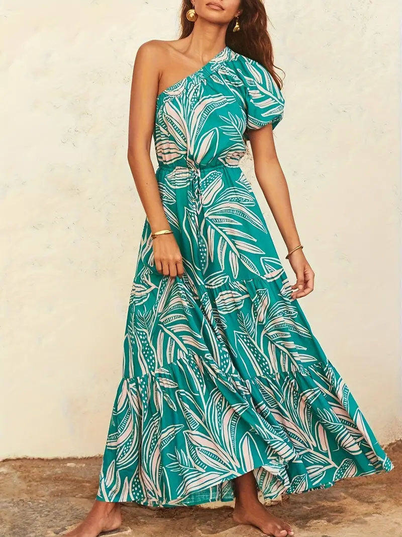Woman wearing a teal one-shoulder tropical maxi dress by FashionRay, barefoot indoors