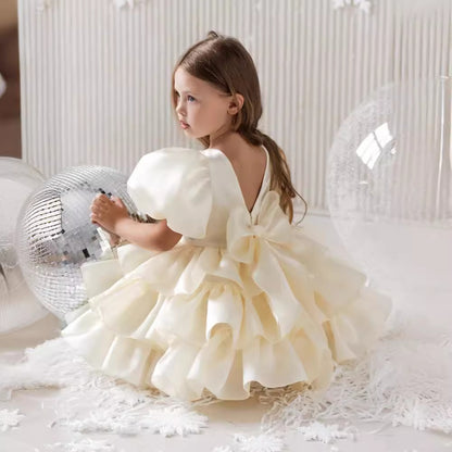 Little girl in ruffled cream dress with bow, sitting by disco ball, FashionRay style photo.