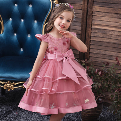 Smiling girl in pink floral dress with bow, posing by blue chair, FashionRay kids fashion