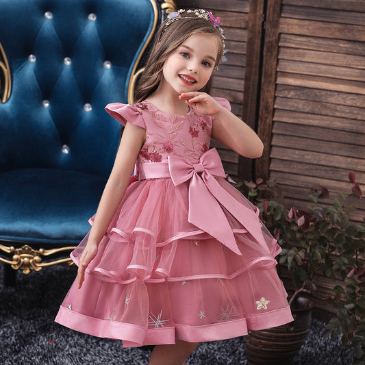 Smiling girl in pink floral dress with bow, posing by blue chair, FashionRay kids fashion