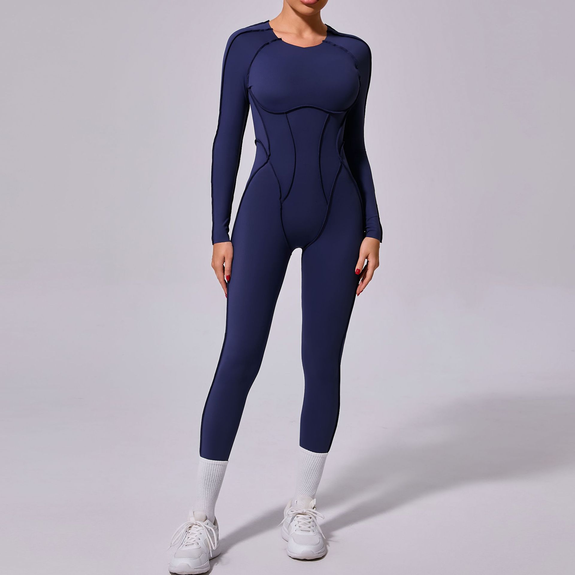 Woman wearing a navy blue long-sleeve jumpsuit and white sneakers, fashionable activewear.