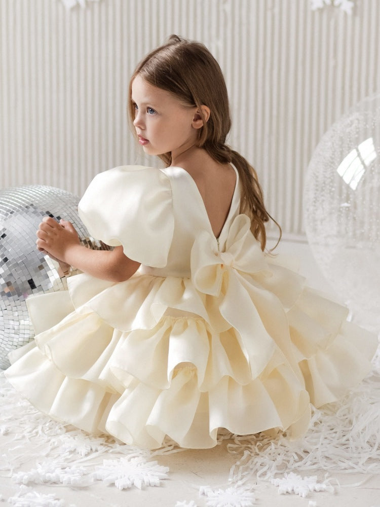 Little girl in a ruffled cream dress with large bow, sitting by disco balls, FashionRay style