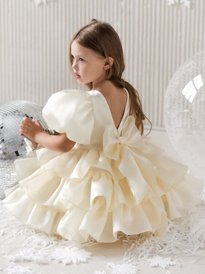 Little girl in a ruffled cream dress with large bow, sitting by disco balls, FashionRay style