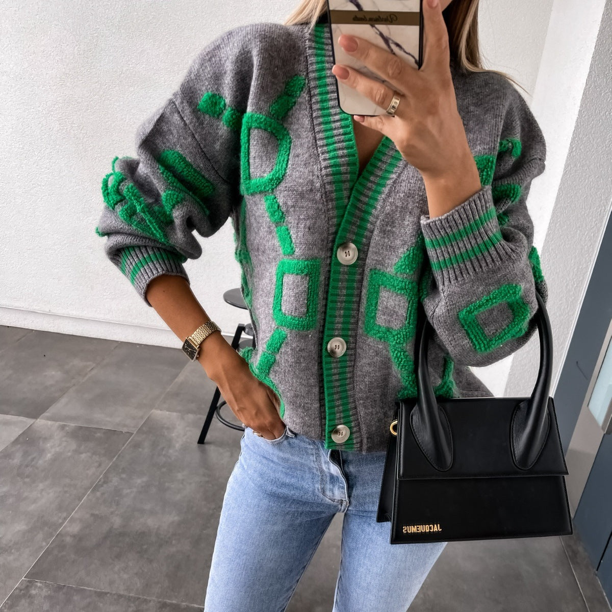 Woman wearing a gray and green patterned cardigan, light jeans, and holding a black handbag, FashionRay style.