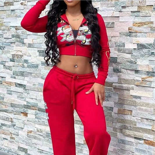 Woman modeling red FashionRay tracksuit set with graphic crop hoodie and jogger pants against stone wall.