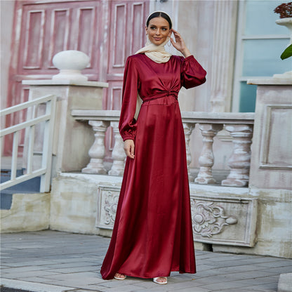 Woman in elegant maroon satin maxi dress with long sleeves, beige scarf, standing outdoors