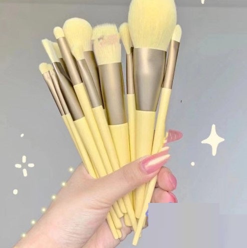 Hand holding a set of yellow makeup brushes, trendy beauty tools at FashionRay