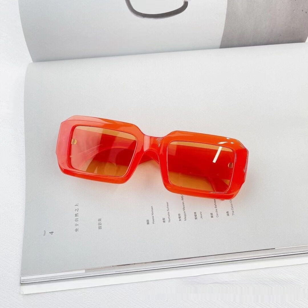 Bold red square sunglasses on open book, trendy eyewear by FashionRay