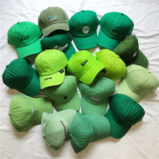 Assorted green baseball caps with trendy embroidered text, displayed on white fabric, FashionRay