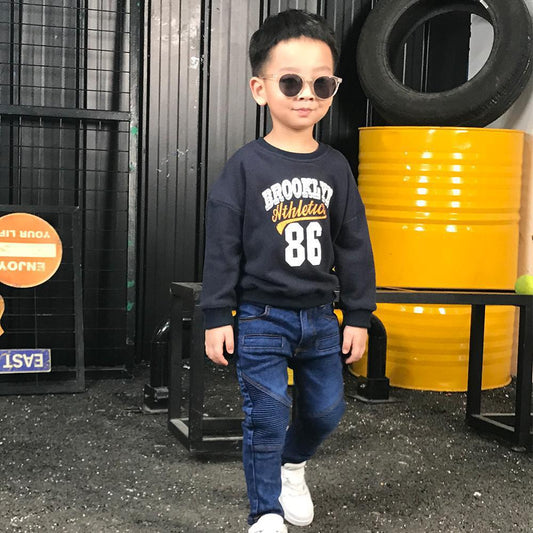 Stylish boy in sunglasses, navy Brooklyn Athletics sweatshirt, jeans, and white sneakers at FashionRay