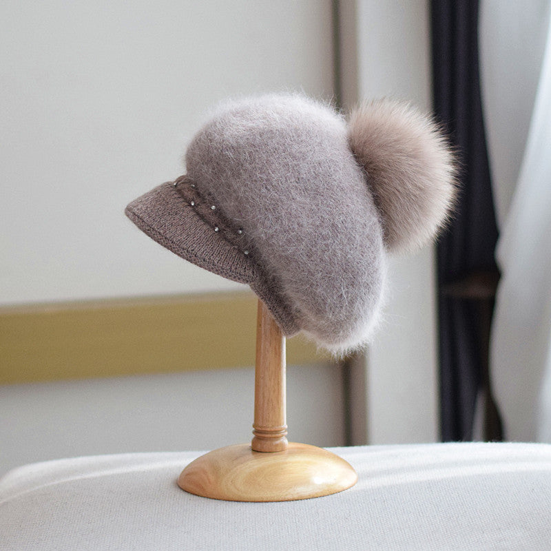 Fluffy brown knit cap with pom-pom and pearl accents on display stand, FashionRay style