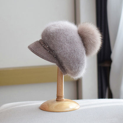 Fluffy brown knit cap with pom-pom and pearl accents on display stand, FashionRay style