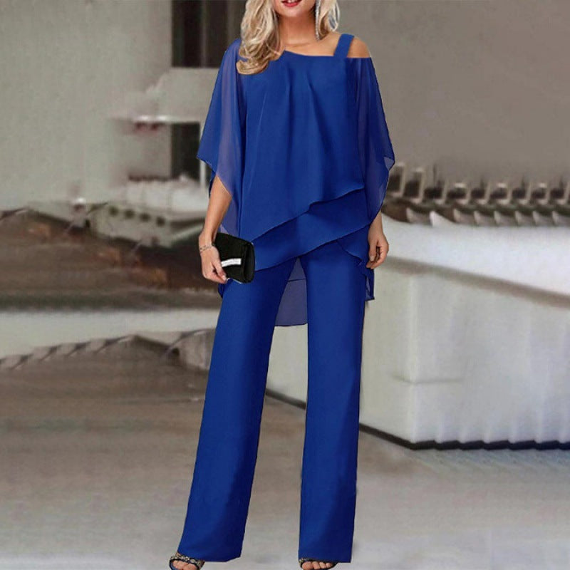 Woman in chic royal blue layered top and pants outfit, holding a black clutch, FashionRay style