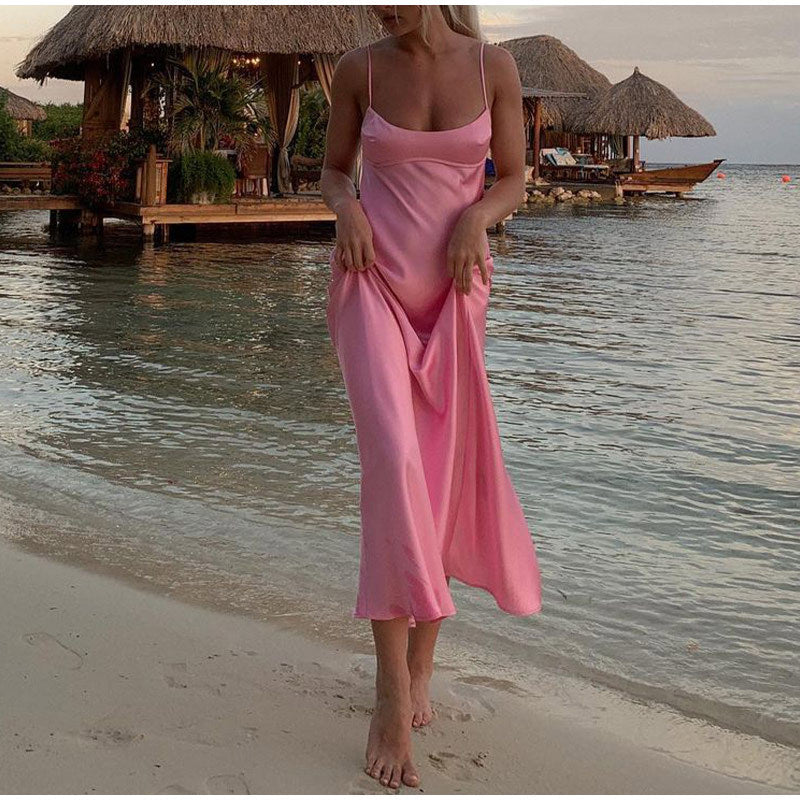 Woman in pink slip dress walking on beach near tropical huts, FashionRay summer style