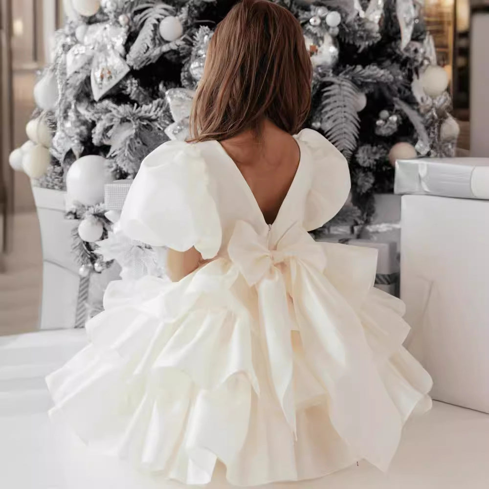 Girl in ruffled white dress with bow sitting by decorated Christmas tree, FashionRay style