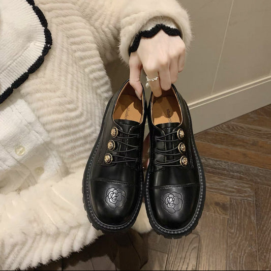 Woman holding black leather fashion loafers with gold buttons and floral embossing