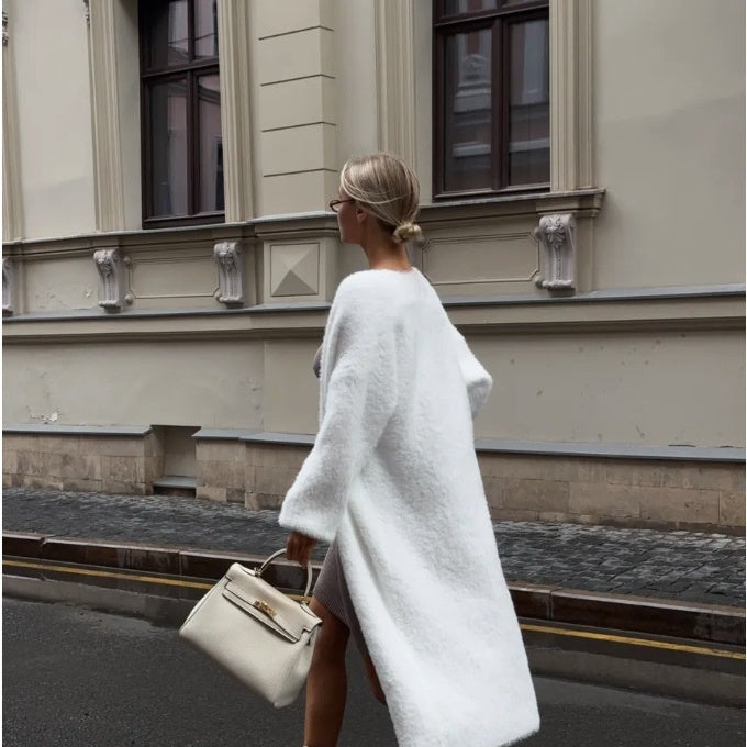 Stylish woman in a white fuzzy coat and sunglasses walking with beige handbag on city street