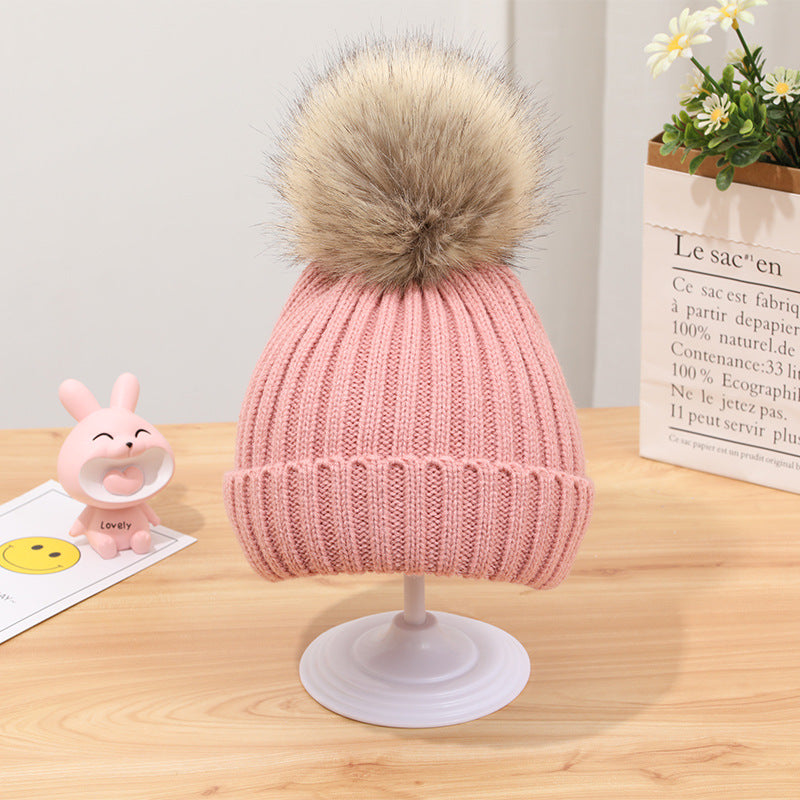 Knit pink beanie with faux fur pom pom, stylish winter hat on display at FashionRay