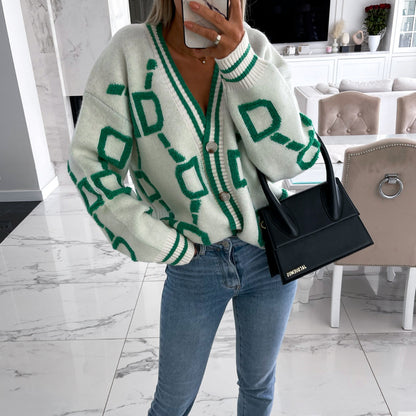 Woman modeling a green geometric cardigan, jeans, and black handbag in a modern living room
