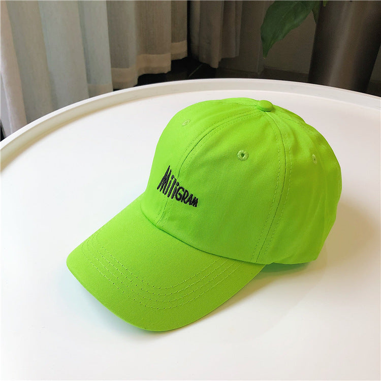 Neon green baseball cap with black 'MIIIGRAM' embroidery on white table, FashionRay trendy style