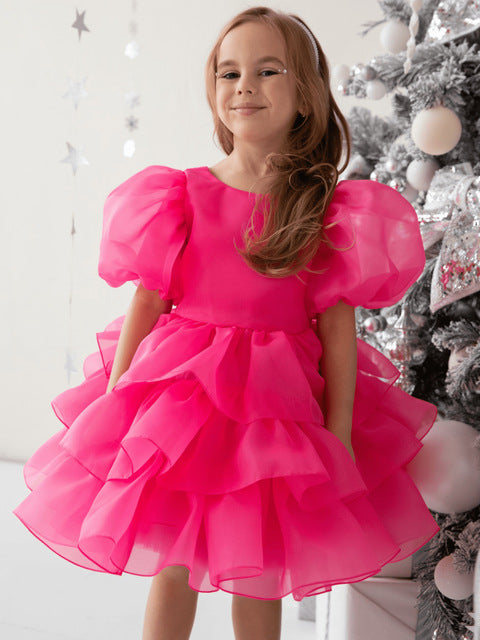 Smiling girl in a bold pink ruffled dress by a decorated Christmas tree, FashionRay style